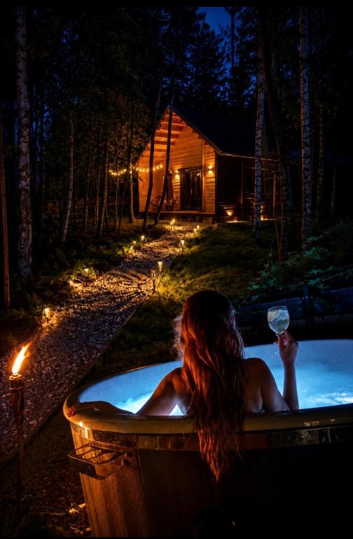 a woman sitting in a bath tub with a glass of wine at DOMEK W BRZOZACH JacuzziBalia w cenie Las Blisko Jeziora in Lgiń