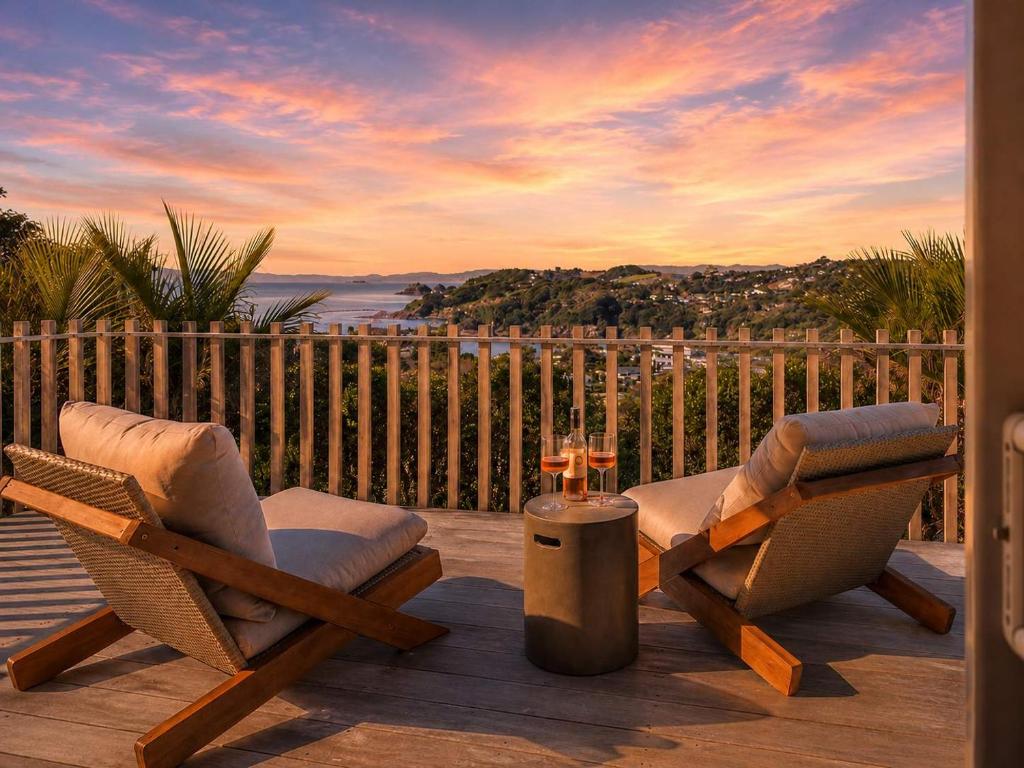 two chairs and a table on a deck with a sunset at Oneroa Vines and Views- Stay Waiheke in Blackpool