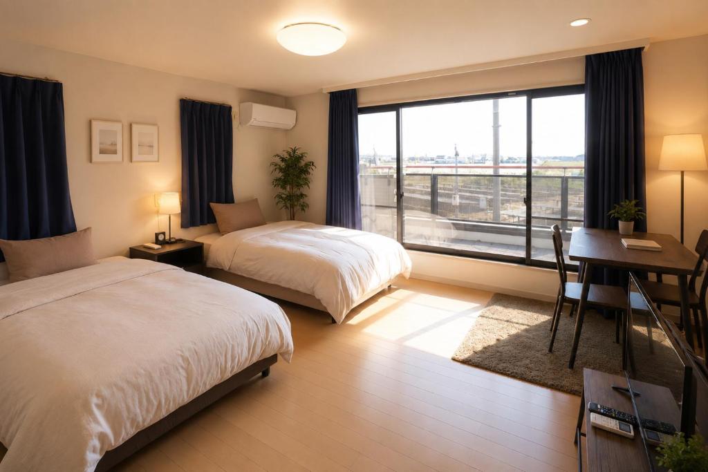 a bedroom with two beds and a desk and a window at ゲストハウスガーデンズmihama in Wada