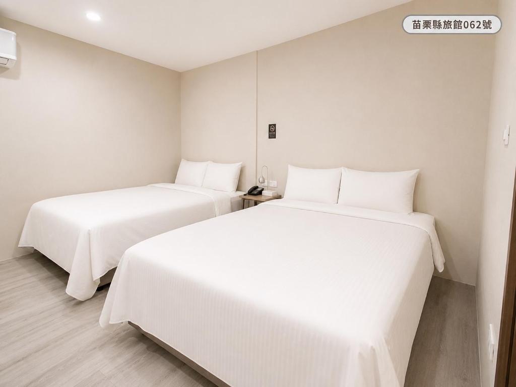 two beds in a room with white sheets at WE Hotel in Miaoli