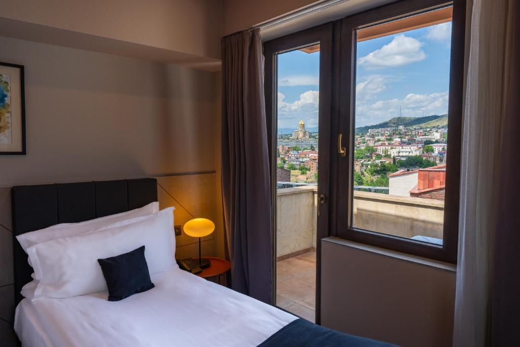 a bedroom with a bed and a window with a view at King Tamar Hotel By Luxuria Hotels in Tbilisi City