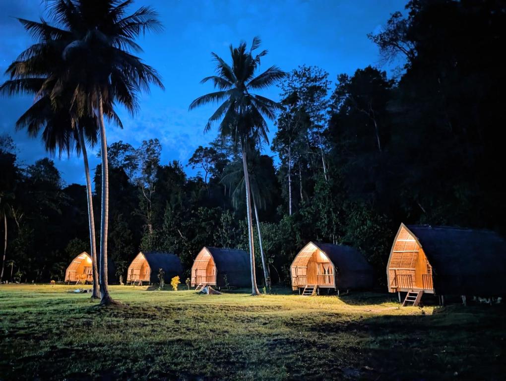 a group of huts and palm trees in a field at Tanjung Kalemo Resort in Batudaka