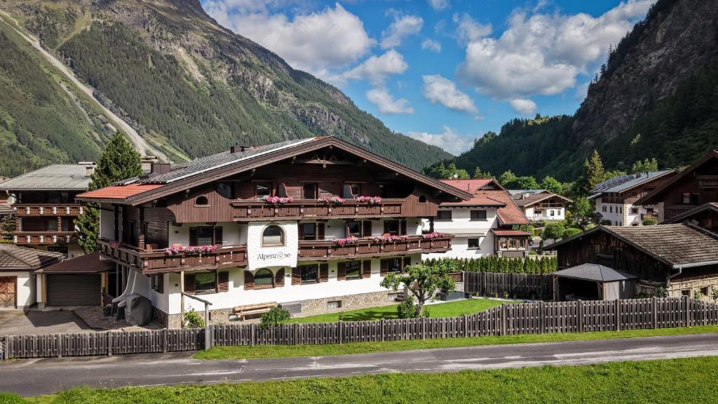 a building in a village with mountains in the background at Appartements Alpenrose in Längenfeld