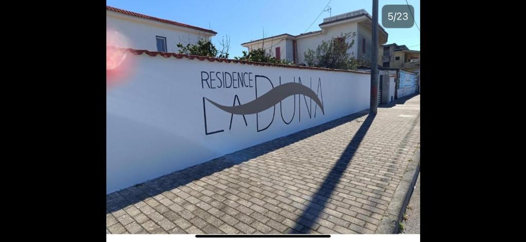 a white wall with a sign on it next to a sidewalk at Residence la Duna in Castel Volturno