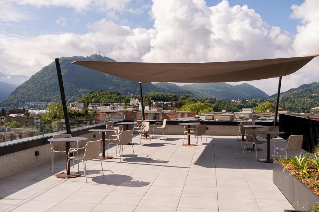 a patio with tables and chairs on a roof with mountains at THE FLAG Lugano - Self Check-in in Massagno