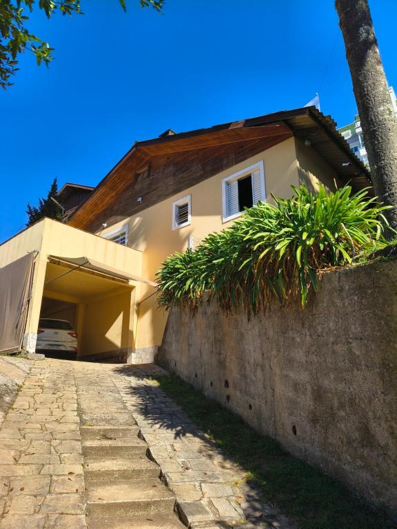a house with a stone wall next to a driveway at Refúgio da Serra - com lareira - 900m do Capivari in Campos do Jordão