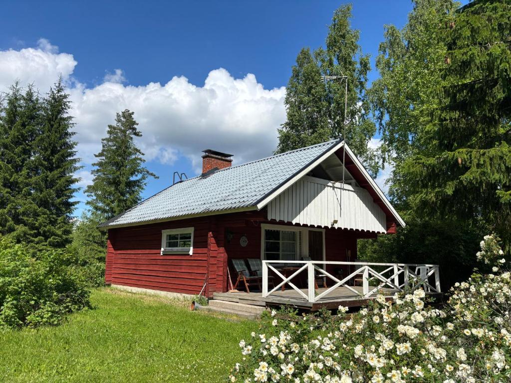 a red cabin in a field with trees and flowers at Villa Metsätähti Punkaharjulla in Vuoriniemi