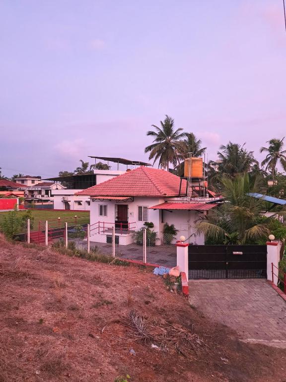 a white house with a red roof and palm trees at Benny's Abode by UrbanEase Properties in Mangalore