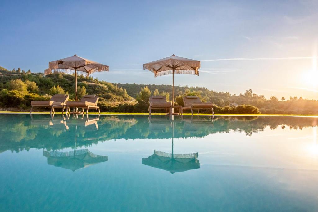 a pool with chairs and umbrellas in the water at Kallies villas with shared Pool in Pefkochori