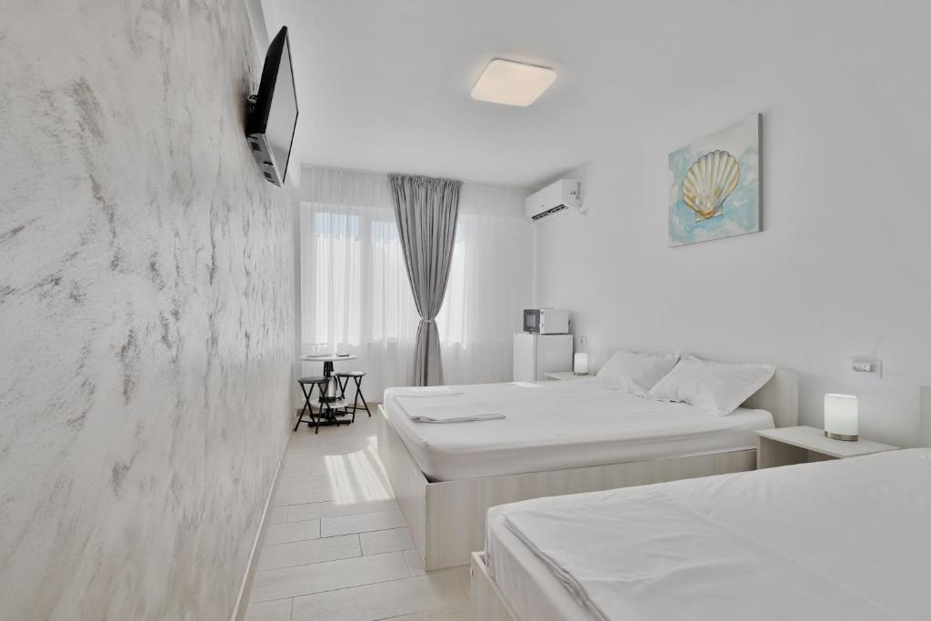 a white bedroom with two beds and a window at Neptune Breeze in Neptun