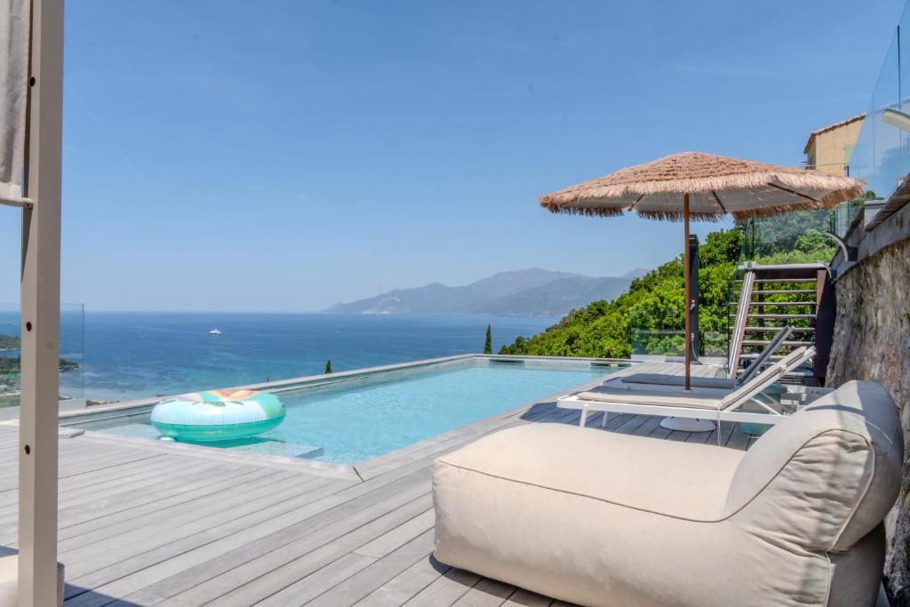 a swimming pool with an umbrella and a couch and a chair at Villa ROYA in Saint-Florent
