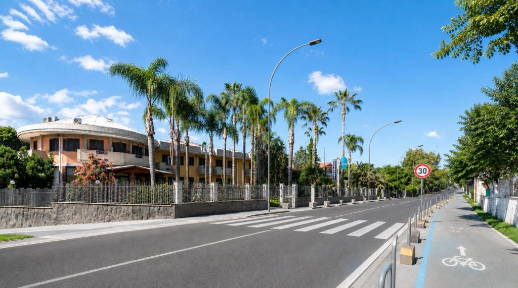 an empty street with a building and palm trees at Oasi Park Hotel in Mascali
