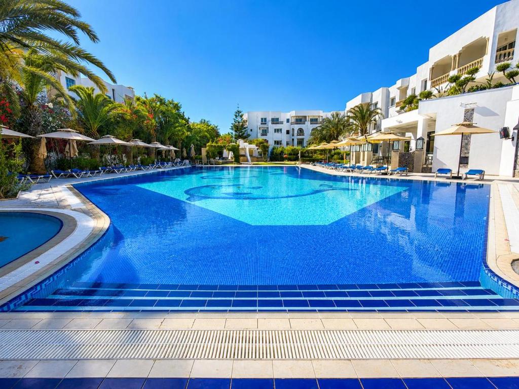 a large swimming pool with palm trees and buildings at Le Corail Apart'Hotel & Splash Park in Hammamet