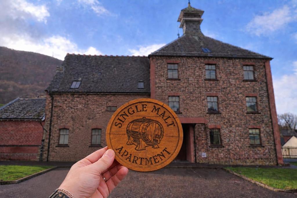 a person holding up a wooden disc in front of a building at Single Malt Apartment in the old distillery in Inverlochy