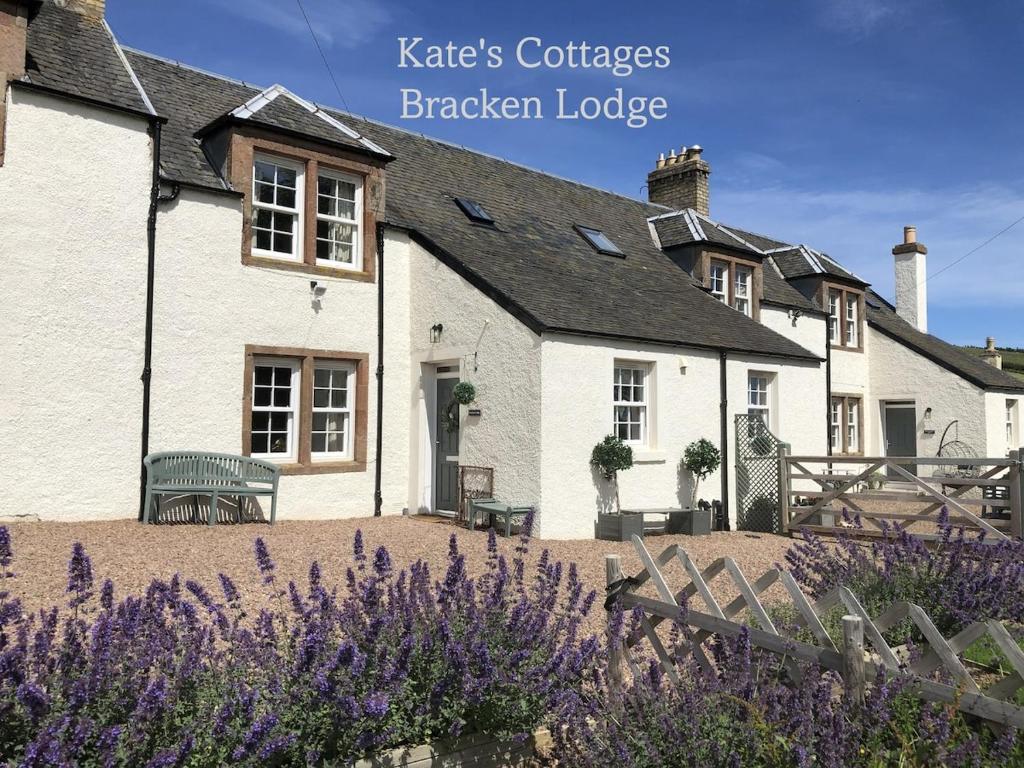 a white house with purple flowers in front of it at Kates Cottages Bracken Lodge in Spott