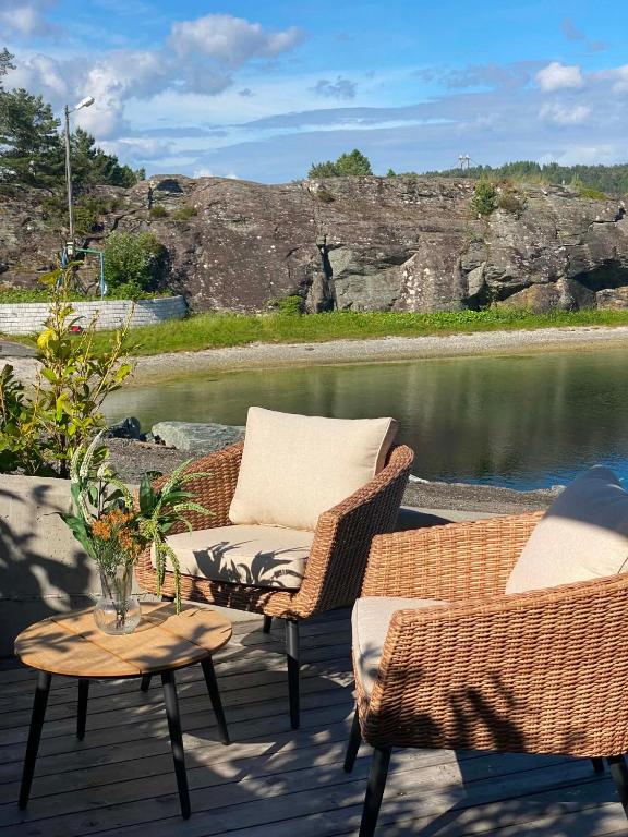 two wicker chairs and a table on a deck with water at Bird Nest in Bømlo
