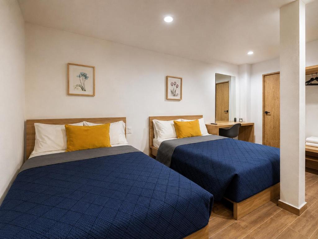 a bedroom with two beds with blue sheets and yellow pillows at Aloja Rentals Mexico in Mexico City