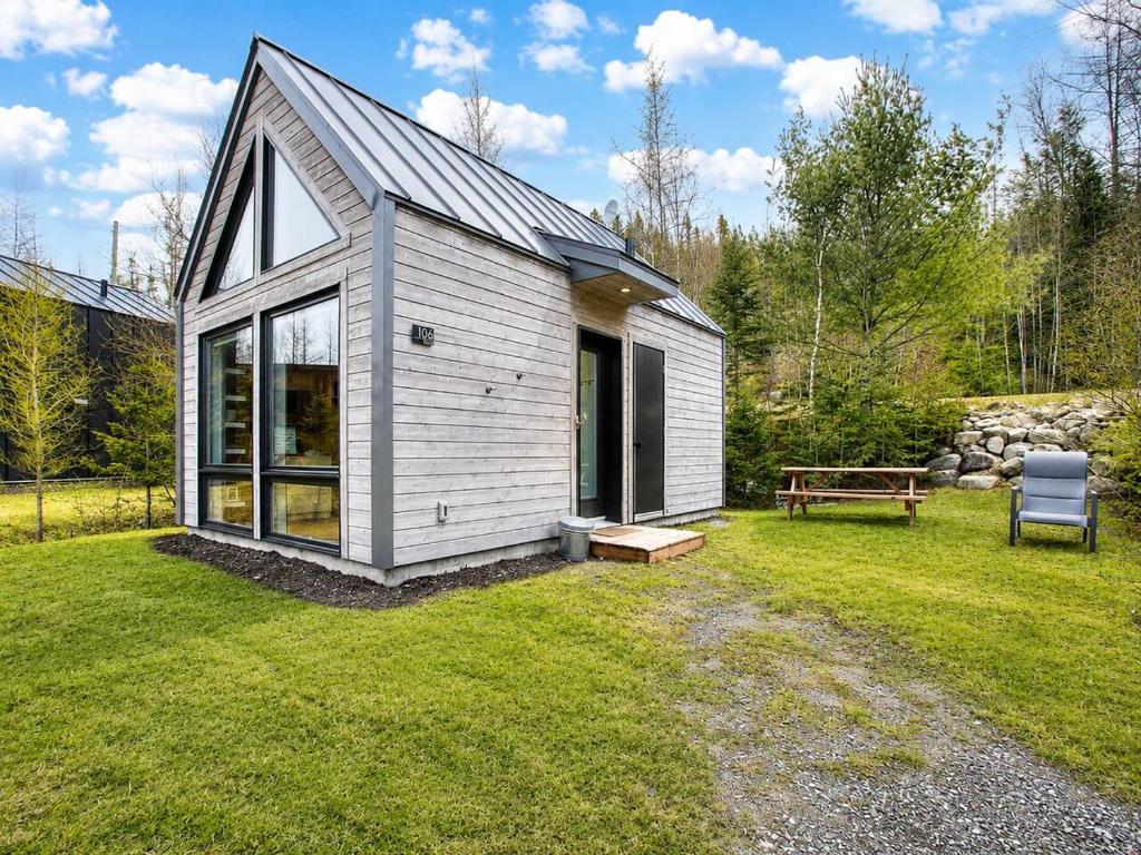ein kleiner weißer Schuppen mit einer Bank in einem Hof in der Unterkunft Nature Getaway with Lake, Horseback Riding & BBQ in Sainte-Marguerite