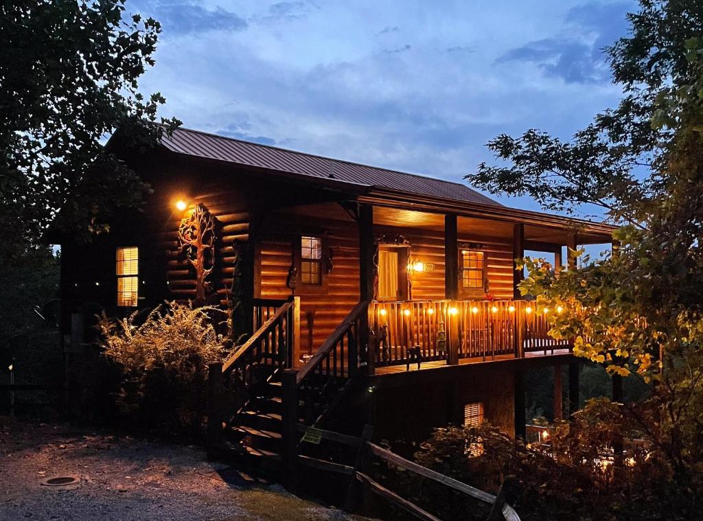 a log cabin with lights on the porch at night at Rustic Cabin, Fire Pit with HotTub, Mountain Views, Peaceful Location in Sevierville