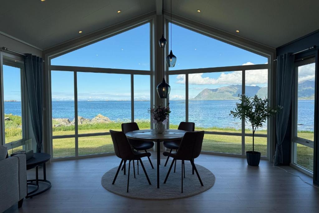 a dining room with a table and chairs in front of windows at Oceanfront Infinity Lodge, Lofoten in Vestvågøya