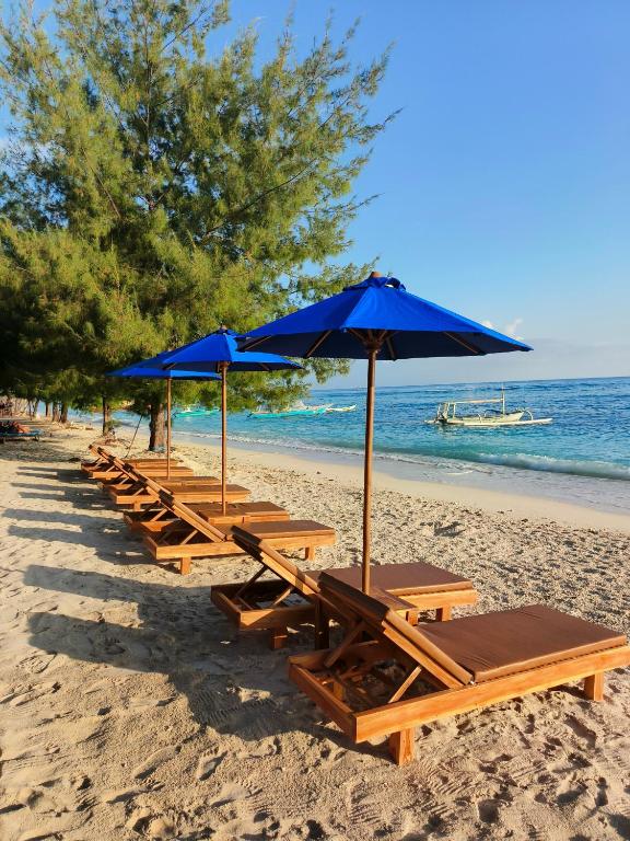a row of picnic tables with blue umbrellas on a beach at Yaya Bungalows Blue Coral in Gili Meno