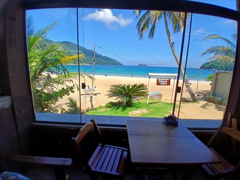 a table and chairs in front of a window with a beach at Aconchego Ebenézer in Praia de Provetá 