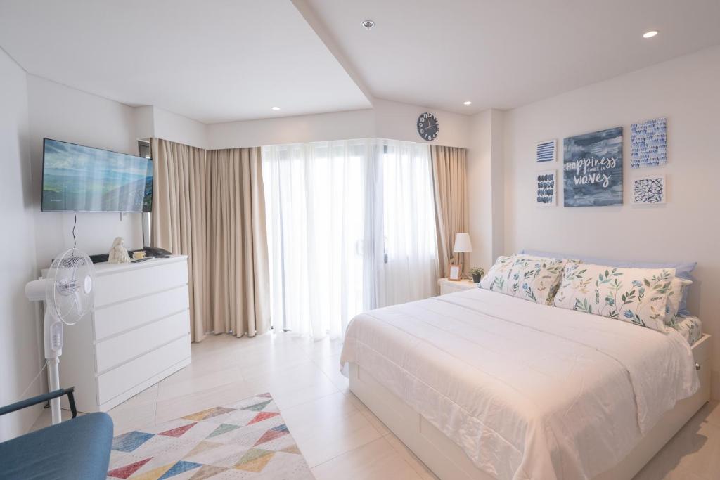 a white bedroom with a bed and a tv at Deluxe Studio-Condo at Tambuli Seaside Living in Maribago