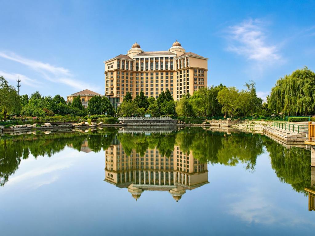a large building is reflected in a lake at 泰安宝龙艺珺酒店 in Tai'an