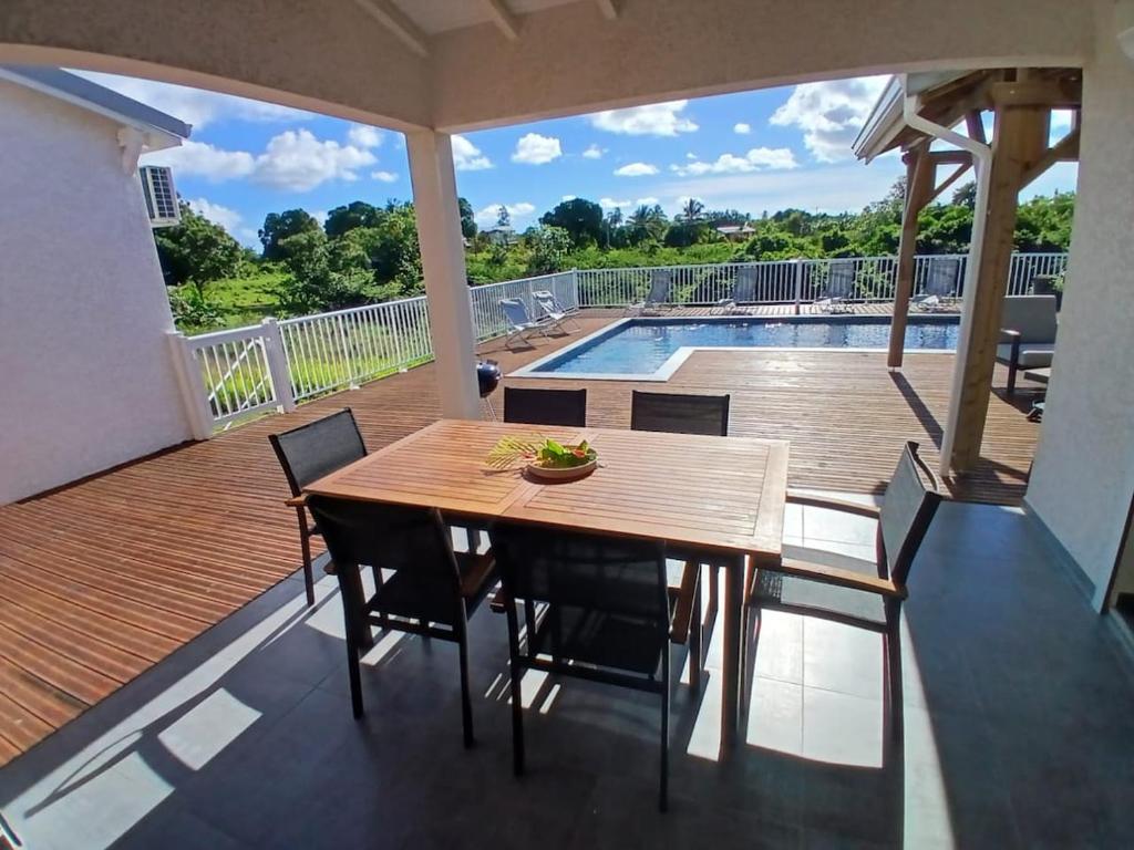 a wooden table and chairs on a deck with a pool at Sun House in Grand-Bourg