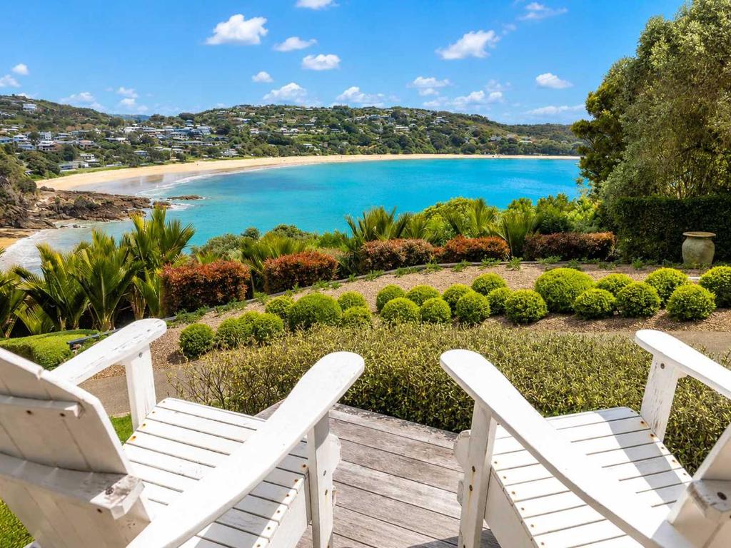 a pair of white chairs on a deck overlooking a beach at Smiths Cottage - Stay Waiheke in Oneroa