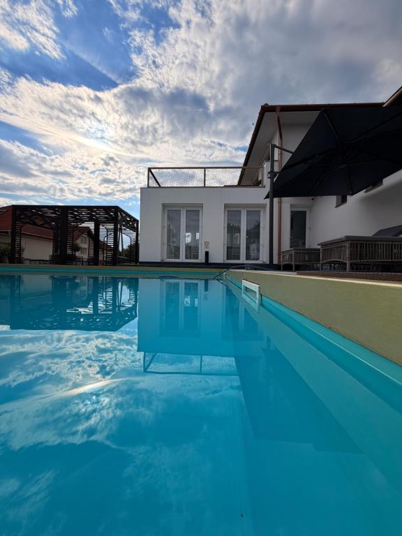 a swimming pool with blue water in front of a house at CasaBlanca vendégház in Abádszalók