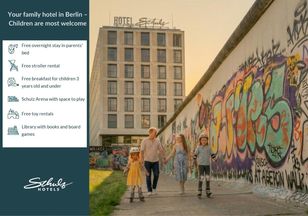 a family walking down a sidewalk in front of a mural at Schulz Hotel Berlin Wall at the East Side Gallery in Berlin