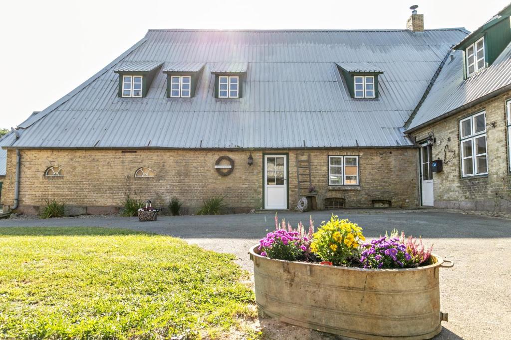 a building with a metal roof and a barrel with flowers at Historischer Resthof in Hövede