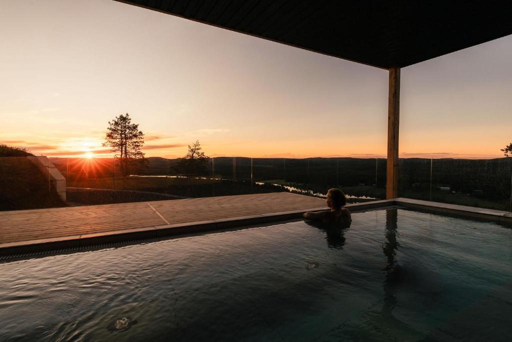 a woman sitting in a swimming pool at sunset at Kaamos Lodge in Aavasaksa