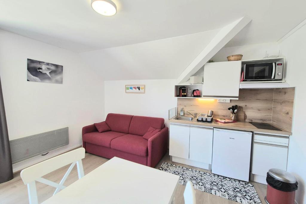 a living room with a red couch and a kitchen at Studio 2 pers avec accès piscine et sauna in Les Déserts