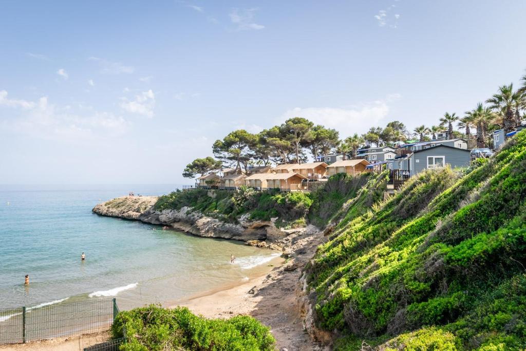 a beach with houses on a hill next to the ocean at Camping Estival Torre de la Mora in Tamarit