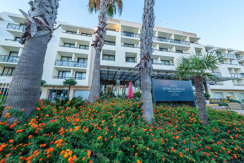a hotel with palm trees and flowers in front of it at Estival Islantilla in Islantilla