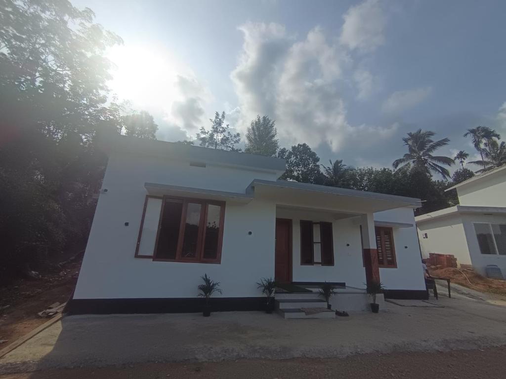 a small white house with trees in the background at Ithal Villa - Home Stay in Wayanad