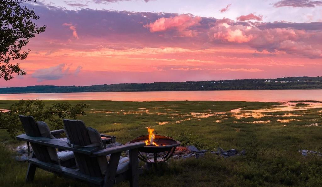 a fire pit with two chairs and a table next to a lake at Condo 1 - Waterfront with SPA, Fireplace & Barbecue in Sainte-Anne-de-Beaupré
