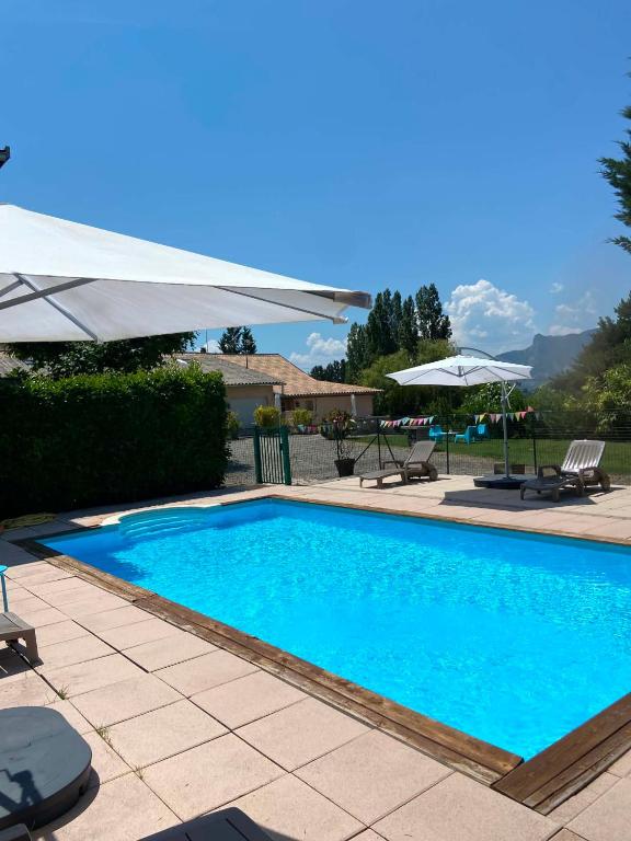 a large blue swimming pool with an umbrella and chairs at Gîtes de La Condamine in Curbans