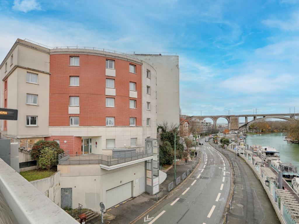 a tall red brick building next to a river at Appart'hotel Vacancéole Paris Quai de Marne in Nogent-sur-Marne