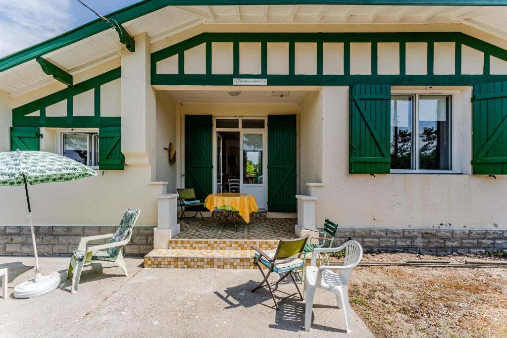 a green and white house with chairs and a table at Maison de Charme in Mimizan-Plage