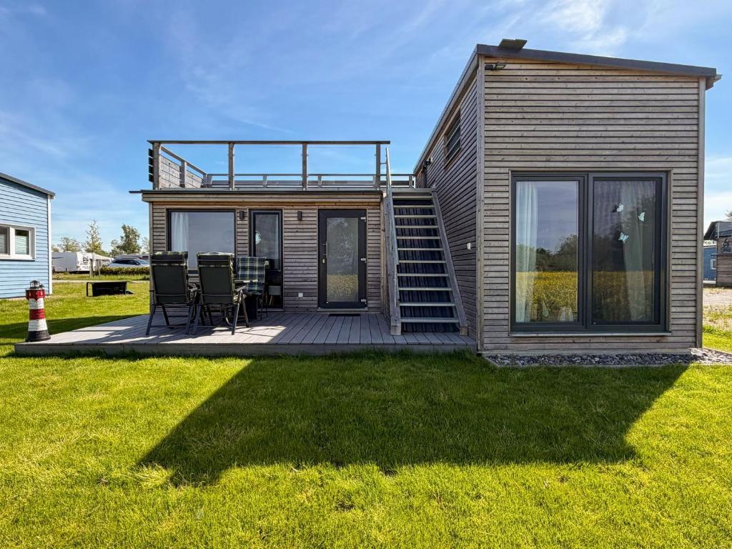 a small cabin with a deck and chairs on the grass at Tiny Haus Schwalbe in Groß Kordshagen