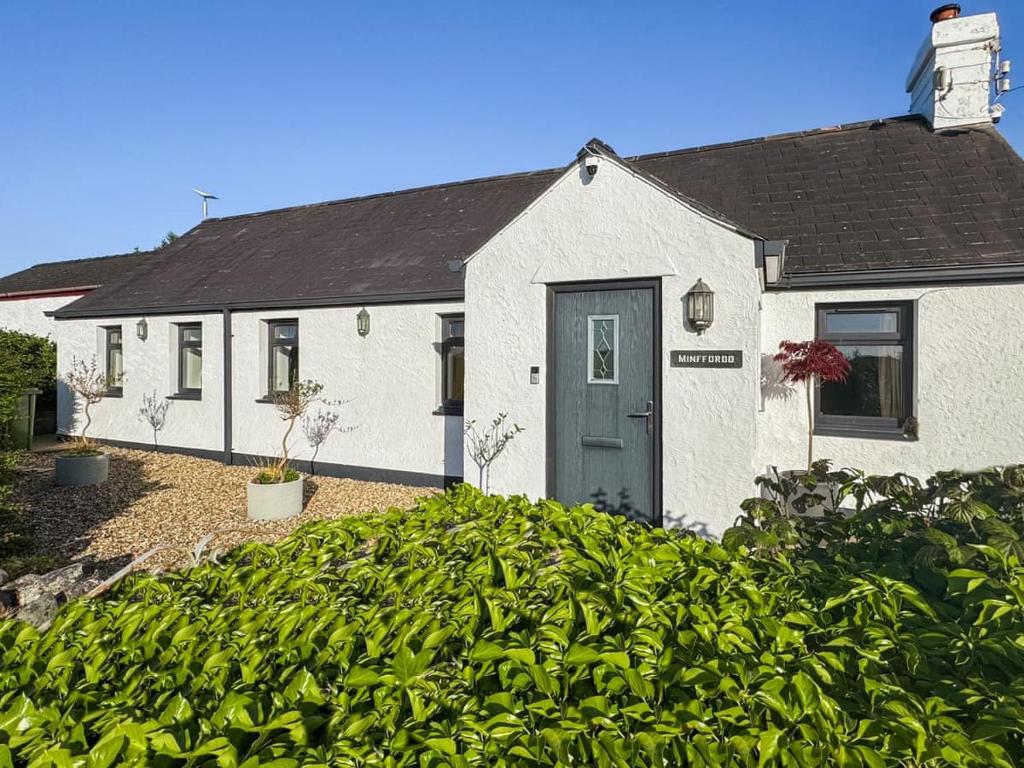 a white house with a blue door and some bushes at 4 Bed in Dothan Ty Croes oc-m44701 in Llanfaelog