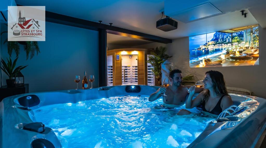 a man and woman sitting in a hot tub at Villa de rêve - Climatisation - Sauna - Spa - babyfoot - Arcade in Quatzenheim