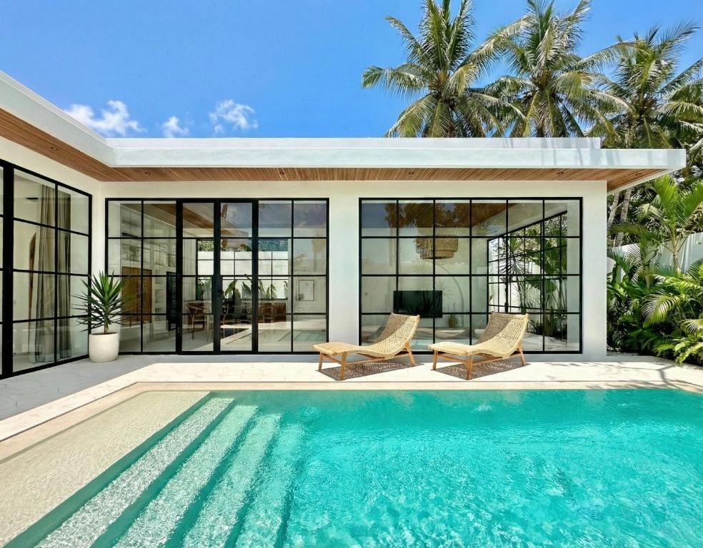 a swimming pool in front of a house with windows at Melrose x The Young Villas in Uluwatu