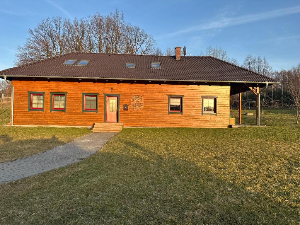 a brown house with a black roof on a grass field at Medová chaloupka in Černá Voda