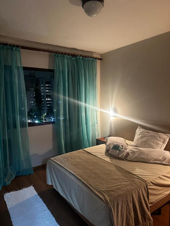 a bedroom with a bed and a window with green curtains at Apartamento Saint Moritz flat service in São Bernardo do Campo