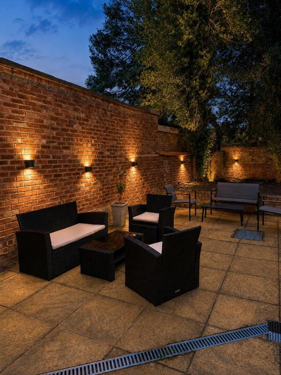 a patio with couches and tables and a brick wall at Historic High St Flat with Peaceful Garden Retreat in Stony Stratford
