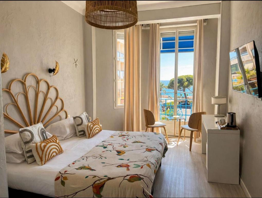 a bedroom with a bed and a table and a window at Hôtel Eden - La Baigneuse in Juan-les-Pins